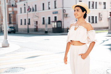 Obraz premium Young beautiful smiling hipster woman in trendy summer costume clothes. Carefree female posing in the street at sunny day. Positive model outdoors at sunset. Cheerful and happy in hat