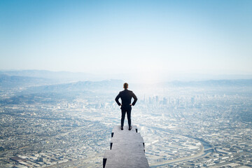 Back view of young man standing on edge and looking at bright blue city sky with mock up place....