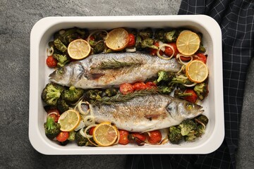 Delicious fish with vegetables and lemon in baking dish on grey textured table, top view