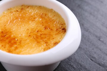 Delicious creme brulee in bowl on dark gray textured table, closeup