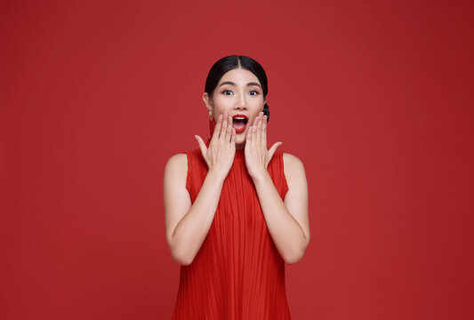 Shocked excited Beautiful Asian woman with mouth open dressed in red cloth isolated on red background