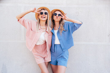 Two young beautiful smiling hipster female in trendy summer clothes. Sexy carefree women posing in th street. Positive models having fun, hugging at sunset. In hat and sunglasses