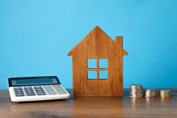 House model, calculator and stacked coins on wooden table against light blue background