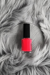 Bright nail polish in bottle on grey faux fur, top view