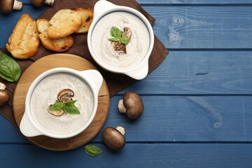 Delicious mushroom soup in ceramic pots and fresh ingredients on blue wooden table, flat lay. Space for text