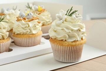 Tasty Easter cupcakes in box on wooden table, closeup