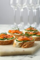 Tasty canapes with salmon, cucumber and cream cheese on white marble table, closeup