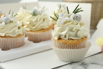 Tasty Easter cupcakes with vanilla cream on white marble table