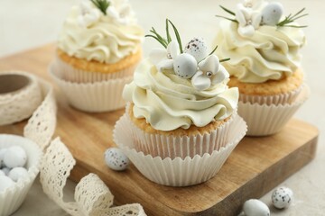 Tasty Easter cupcakes with vanilla cream, candies and ribbon on gray table, closeup