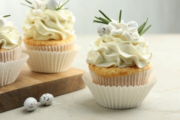 Tasty Easter cupcakes with vanilla cream and candies on gray table