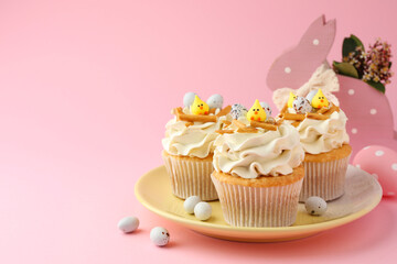 Tasty Easter cupcakes with vanilla cream and candies on pink background, space for text