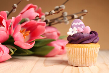 Tasty decorated Easter cupcake, flowers and willow branches on wooden table