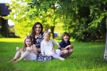 Obraz premium Young large family on a summer morning walk. Beautiful mother with children is playing in the park.