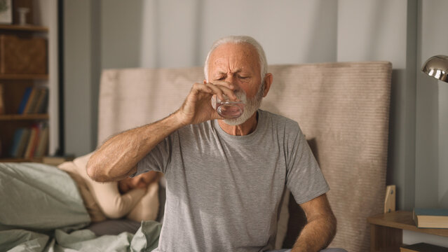 Elderly man drinking glass of water in bed