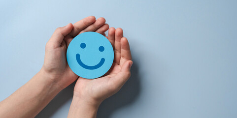 paper cut smiley face in hands on light blue background. positive thinking, mental health,...