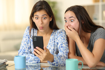 Amazed women checking smart phone at home