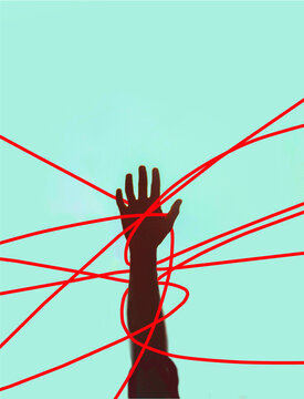 Hand of unrecognizable person tangled in red strings against colored background