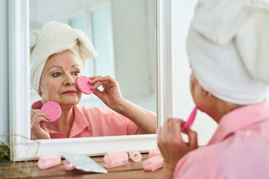 Woman wearing towel and taking care of skin looking in mirror at home