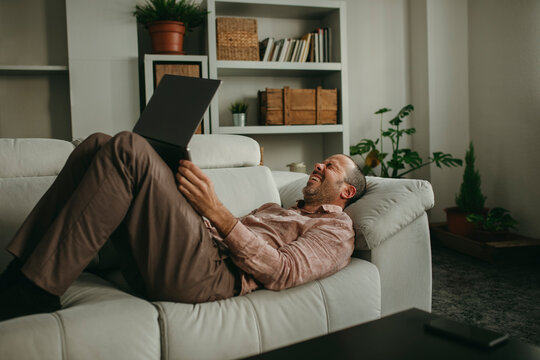 Cheerful man lying down and watching movie on laptop at home