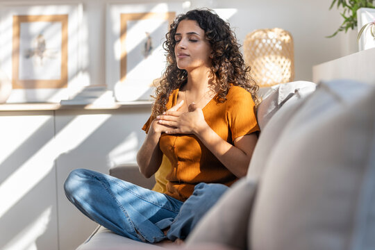 Young woman meditating with hands on chest at home