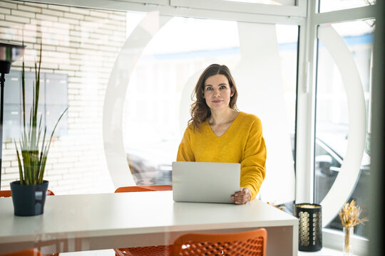 Confident creative businesswoman with laptop at table in office