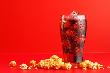 Cola with ice over red background