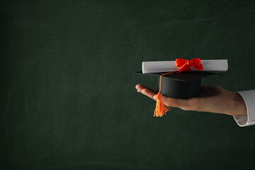 Miniature graduate hat and diploma, in hands.