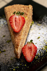 layer sponge cake with strawberries on a black plate on wooden background