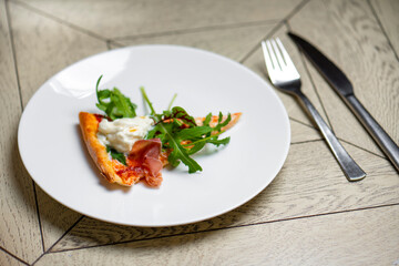 piece of pizza with smoked salmon and arugula on a white plate