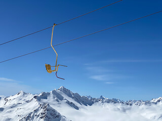 A yellow seat of skiing lift in the mountains on a blue sky background