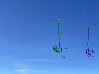 Colorful seats of skiing lift in the mountains on a blue sky background, transportation to the top