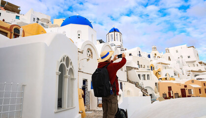 Young tourist man backpack using smartphone take picture at View of blue church dome in Oia...