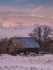 An old wooden shed in a village under snowy peaks in a valley of fog. Romantic winter landscape. Hrabusice Slovak Paradise High Tatras.