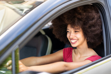 Cheerful woman with Afro hair driving automobile