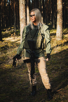 Beautiful military girl with a modern AK 12 suppressed rifle and pistol in the forest. Vertical photo.