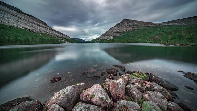 The mountains covered with dense forests are beautifully mirrored in the calm and serene shallow lake. A timelapse video.