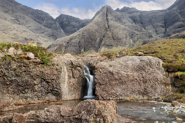 A solitary waterfall tumbles into the tranquil Fairy Pools, embraced by the craggy grandeur of the...