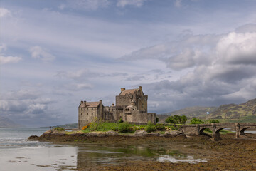 Eilean Donan Castle reflects its storied past in the calm loch, flanked by a historic bridge and the undulating hills of the Scottish Highlands
