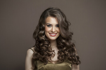 Naklejka premium Beautiful woman with long healthy wavy hair, cute smile and make-up looking at camera on brown studio wall background, fashion beauty portrait