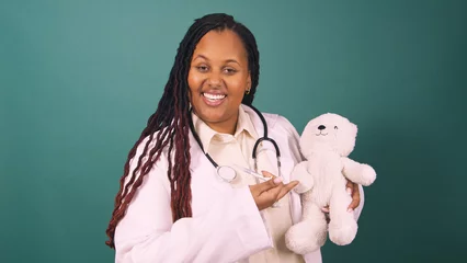 Ingelijste posters Young Black female doctor demonstrates an injection, using teddy bear © Meeko Media