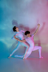Male and female ballet dancers in matching outfits executing complex dance move with grace in neon...