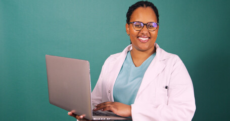 Young Black female doctor works on laptop, smiles at the camera