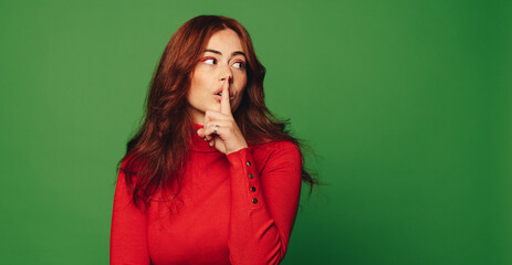 Young woman making shush gesture on a green background