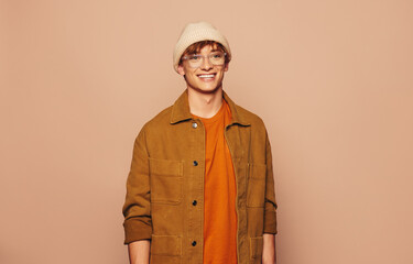 Smiling man in stylish urban denim jacket and glasses standing on vibrant peach background - 773852602