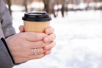 Close-up of male hands holding paper cup with coffee on snow background.