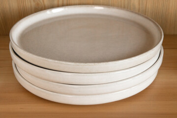 A stack of beige ceramic plates in a wooden cupboard.