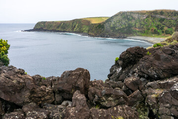 Scenic view of volcanic rock bay on Terceira Island, Azores. Dramatic landscape with rugged cliffs and clear blue waters. Perfect for travel and nature themes.