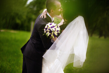 A couple in a wedding dress and with a bouquet of flowers kiss in the park