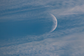 Moon behind white clouds in blue sky at day