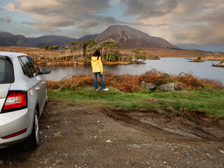 Teenager girl in yellow tourist jacket standing by silver car. Twelve pine island and stunning...